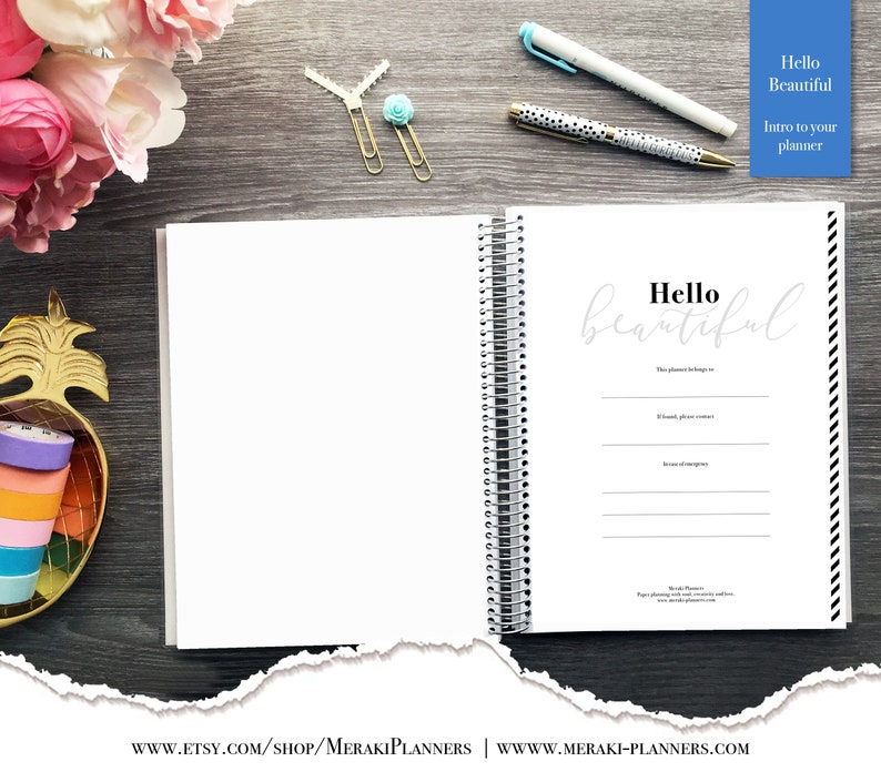 May include: Open spiral-bound planner with the words "Hello Beautiful" on the inside page. The planner is white with black and white striped edges. A gold pineapple-shaped container holds colorful washi tape.