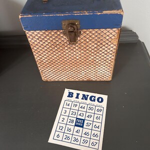 May include: A vintage bingo set featuring a blue and tan patterned box with a clear handle and a metal clasp. A bingo card with the word "BINGO" at the top and numbered squares is also visible.