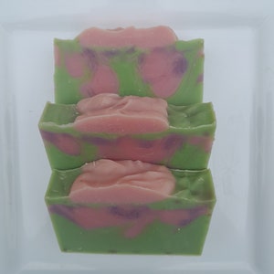 May include: Three bars of handmade soap with a green and pink swirl pattern. The soap is stacked on top of each other.