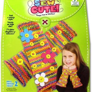 Puede incluir: Un kit de manualidades con el texto "SEW CUTE!" presenta calentadores de brazo de punto coloridos decorados con botones y aplicaciones de flores. El kit incluye instrucciones para hacer dos pares de calentadores de brazo. Los calentadores de brazo se muestran en una persona joven.