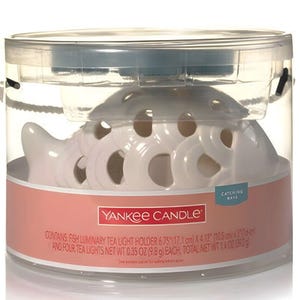 May include: White ceramic fish-shaped tea light holder with cut-out designs. The holder comes with four tea lights. The packaging reads "Yankee Candle" and "Catching Rays".
