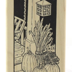 May include: A black and white illustration of a porch scene with a lantern, pumpkins, and a bundle of corn stalks.