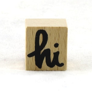 Op de afbeelding: Een houten stempel met het woord "hi" in zwarte inkt.