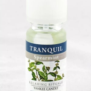 May include: A small glass bottle of Tranquil Spearmint Home Fragrance Oil by Yankee Candle. The bottle is clear and has a white cap. The label is blue and white and features a sprig of spearmint. The text on the label reads "Tranquil Spearmint", "Relaxing Rituals", "Yankee Candle", "Home Fragrance Oil", and "Net Wt 0.33 fl oz (10ml)".