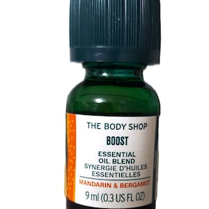 May include: A green glass bottle with a green cap containing The Body Shop Boost Essential Oil Blend, a blend of mandarin and bergamot essential oils. The bottle is labelled with the text "The Body Shop Boost Essential Oil Blend Synergie d'Huiles Essentielles Mandarin & Bergamot 9 ml (0.3 US FL OZ)".