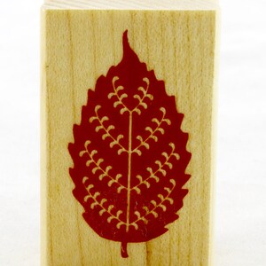 May include: A wooden stamp featuring a red leaf design. The leaf has a detailed pattern of small lines and curves.