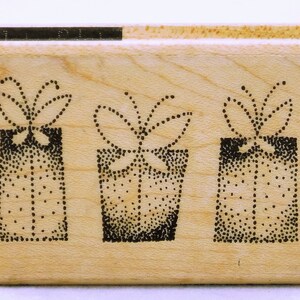 May include: A wooden stamp with three black and white illustrations of gift boxes with bows. Each box is filled with small dots.