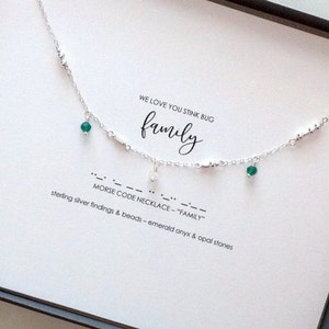 May include: A silver chain necklace with green gemstone beads and silver charms spelling out "family" in Morse code. The necklace comes in a white box with the text "WE LOVE YOU STINK BUG family MORSE CODE NECKLACE - "FAMILY" sterling silver findings & beads - emerald onyx & opal stones."