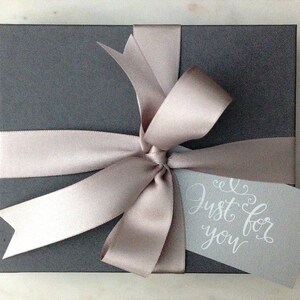 May include: A gray gift box with a light brown satin ribbon tied in a bow. A white tag with the text "Just for you" is attached to the ribbon.