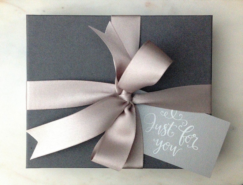 May include: A gray gift box with a light brown satin ribbon tied in a bow. A white tag with the text "Just for you" is attached to the ribbon.