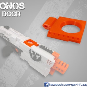 Può includere: Un blaster Nerf Rival Kronos bianco e arancione con un accessorio per porte di inceppamento arancione stampato in 3D. Il testo "KRONOS JAM DOOR" è visualizzato in testo nero su sfondo bianco. Il testo "RIVAL" è visibile sul blaster. Il testo "facebook.com/gavinfuzzycustoms" è visualizzato in testo bianco su sfondo blu.