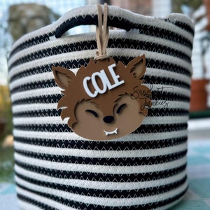 Może przedstawiać: Koszyk do przechowywania w czarno-białe paski z brązową, wilczą etykietą z napisem "COLE".