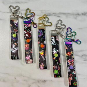 May include: Five colorful Halloween-themed keychains with Mickey Mouse ears. Each keychain features a black background with colorful cartoon images of Halloween treats, characters, and symbols.