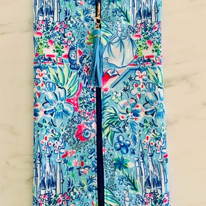 May include: A blue zippered pouch with a colorful floral and castle pattern. The design includes a Cinderella illustration and a blue tassel zipper pull. The pouch is rectangular and likely made of fabric.