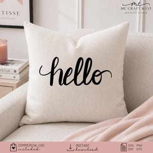 May include: A square off-white throw pillow featuring the word hello written in a black cursive script font centered on the front. The pillow has a textured fabric appearance and is positioned on a light-colored sofa with a soft pink blanket.