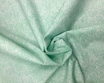 Puede incluir: Primer plano de una tela con un patrón floral repetitivo en verde claro y blanco. La tela está recogida y doblada, mostrando la textura y el diseño. El patrón presenta hojas y flores estilizadas.