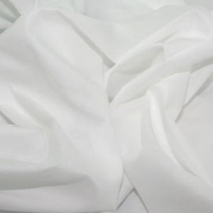 Peut inclure: Gros plan sur un tissu blanc avec des plis et des ombres douces. Le tissu semble léger et fluide, avec un éclat subtil. Les plis créent une sensation de profondeur et de texture, suggérant un matériau délicat.