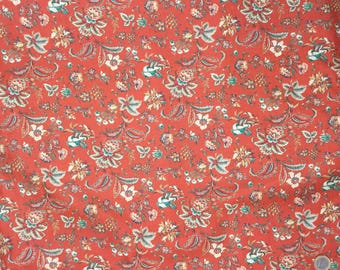 May include: Close-up of a fabric with a repeating floral pattern. The fabric has a red-orange background with a design of flowers, leaves, and paisley shapes in shades of white, teal, and brown. The overall effect is a vintage, botanical theme.