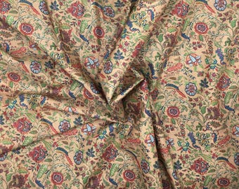 May include: Tan fabric with a detailed floral pattern. The design features red, blue, and green flowers and foliage. The fabric is tightly woven and appears to be cotton or a similar material, suitable for various sewing projects.