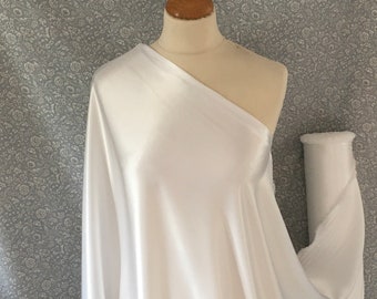 May include: A white fabric draped over a mannequin. The fabric has a smooth, satin-like texture and appears to be a single piece. The background is a floral patterned fabric. A tag with the text "Sigrid's Fabrics" is visible.