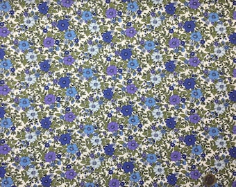 May include: Floral fabric with a repeating pattern of blue and purple flowers and green leaves on a white background. The fabric is densely covered with the floral design, creating a visually rich texture. Ideal for sewing projects.