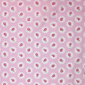 Peut inclure: Tissu rose clair orné d'un motif répété de petites roses rouges dans des cadres blancs festonnés. Les roses ont des feuilles vertes, et le fond est rose clair uni. Parfait pour la couture.