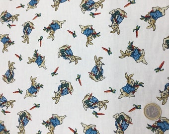 May include: White fabric with a repeating pattern of cartoon rabbits wearing blue striped jackets and holding carrots. The rabbits are in various poses, and orange carrots are scattered across the background.