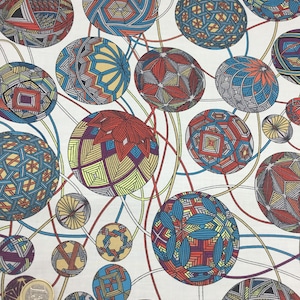Op de afbeelding: Witte stof met een herhaald patroon van kleurrijke, geometrische bollen. De bollen zijn gevuld met ingewikkelde ontwerpen in rood, blauw, geel en paars, verbonden door gebogen lijnen. Een munt is zichtbaar.