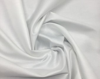 May include: A close-up shot of white satin fabric. The fabric is draped and folded, creating soft shadows and highlights. The material has a smooth, lustrous appearance, suggesting a luxurious texture. The folds and curves of the fabric create a sense of movement and depth.
