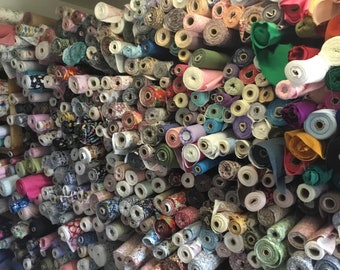 May include: A wall of fabric rolls in various colors and patterns. The rolls are tightly packed together, showcasing a wide array of textiles. The fabrics include floral prints, solid colors, and textured materials, offering a diverse selection for sewing and crafting projects.