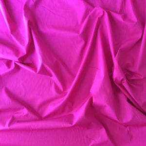 Puede incluir: Una vibrante tela fucsia con pliegues suaves y sombras. El textil tiene una textura suave y un color sólido y brillante. La imagen muestra la caída y el brillo de la tela, lo que sugiere que podría usarse para ropa o decoración del hogar.