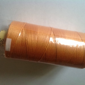 Può includere: Una bobina di filo arancione avvolta in plastica trasparente. Il filo è ben avvolto e un'etichetta con il numero "30/4" è visibile. Il filo è di un colore arancione chiaro e caldo.