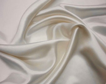 May include: Ivory-colored silk fabric with a lustrous sheen. The fabric is draped, creating soft folds and shadows. The material appears smooth and luxurious, ideal for apparel or home decor projects.