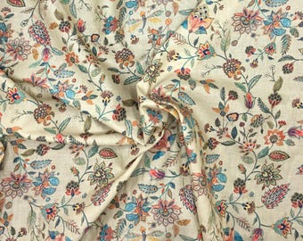 May include: Cream-colored fabric with a detailed floral pattern. The design features various flowers and leaves in shades of blue, orange, pink, and green. The fabric is folded, showing the texture and depth of the material.