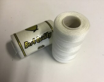 May include: Two spools of white thread. One spool is upright, showing the thread wound around a central core. The other spool is on its side, with the text "Best Quality" and "40/s" visible.