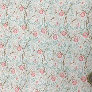 May include: A repeating pattern of pink flowers, light blue leaves, and brown branches on a white background. The floral design is reminiscent of a vintage wallpaper or fabric print. The pattern is dense and covers the entire surface.