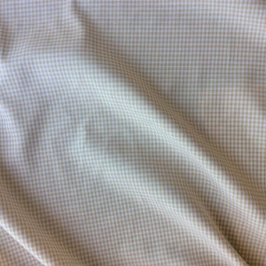 Peut inclure: Gros plan sur un tissu à petits carreaux beiges et blancs. Le tissu est drapé, créant des plis et des ombres douces. Le motif est uniformément espacé, donnant un aspect classique et texturé. Idéal pour l'habillement ou la décoration intérieure.