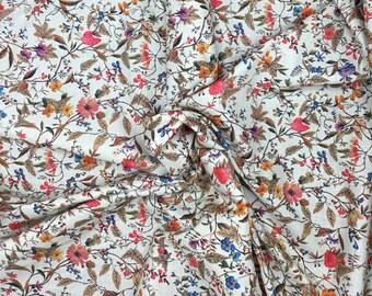 May include: White fabric with a repeating floral pattern. The design features a variety of colorful flowers in shades of pink, orange, blue, and purple, along with brown leaves and stems. The fabric is likely cotton or linen.