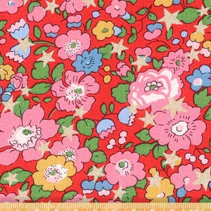 Pode incluir: Tecido floral vermelho com flores rosa, amarelas e azuis, folhas verdes e estrelas douradas brilhantes. Uma régua na parte inferior mostra as medidas em centímetros e polegadas.