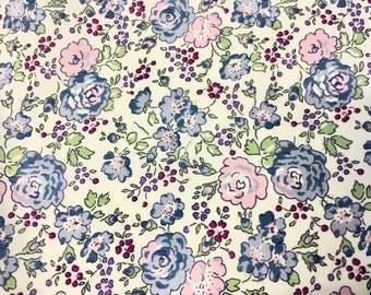 May include: Floral fabric with a cream background. The pattern features blue, pink, and purple roses, along with smaller purple berries and green leaves. The design is repeated across the fabric.