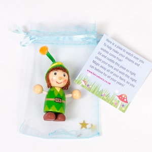 May include: A small wooden pixie doll with green clothing, brown hair, and a yellow hat. The pixie is sitting in a blue and white tulle bag with a note that reads "Here is a pixie to watch over you. To help make your dreams and wishes come true! Sit and cuddle this pixie so tight, close your eyes and wish this night. Magic away all of your fears, so you can believe for all your years! www.fairydoorz.co.uk"