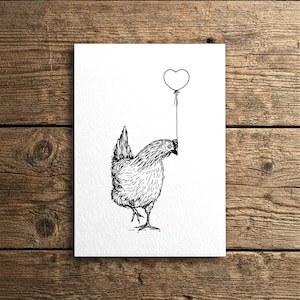 Puede incluir: Ilustración en blanco y negro de una gallina sosteniendo un globo en forma de corazón. El dibujo detallado muestra la gallina con una apariencia texturizada, y el globo está suspendido arriba. La obra de arte está sobre una tarjeta blanca, sobre un fondo de madera.