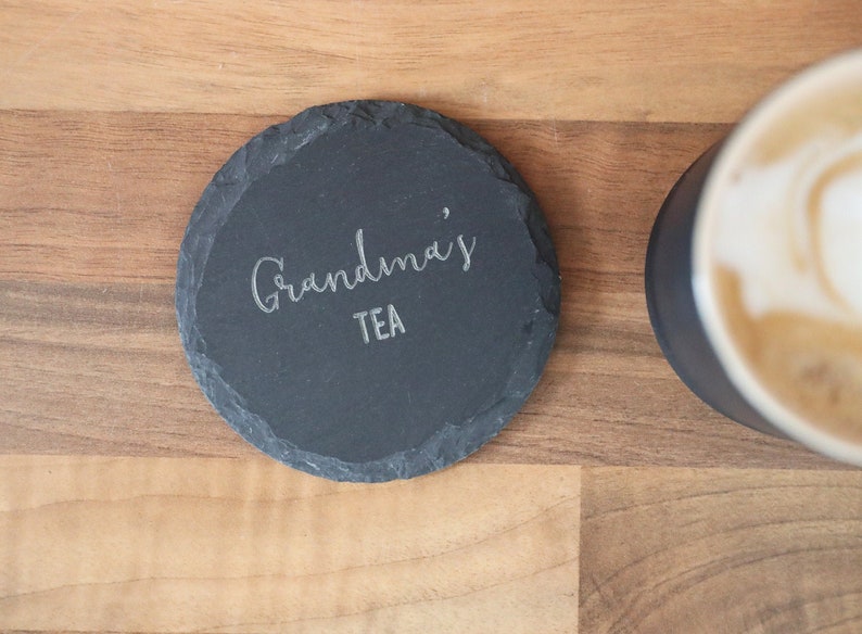 May include: A black slate coaster with the text "Grandma's Tea" engraved in silver lettering.