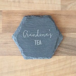 Puede incluir: Un posavasos hexagonal de pizarra con el texto "Grandma's Tea" grabado en blanco.