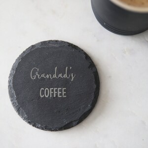 Puede incluir: Un posavasos de pizarra negra con el texto "Grandad's Coffee" grabado en &eacute;l.