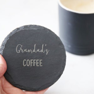 Puede incluir: Un posavasos redondo de pizarra negra con las palabras "Grandad's Coffee" grabadas en blanco.