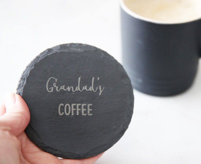 Puede incluir: Un posavasos redondo de pizarra negra con las palabras "Grandad's Coffee" grabadas en blanco.