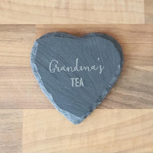 Puede incluir: Un posavasos de pizarra en forma de coraz&oacute;n con el texto "Grandma's Tea" grabado en &eacute;l.