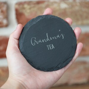May include: A black slate coaster with the text "Grandma's Tea" engraved in white.
