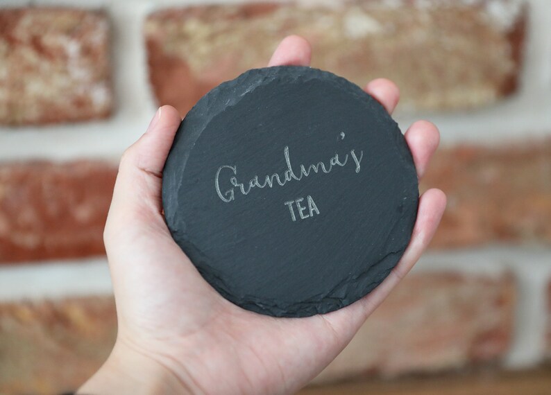 May include: A black slate coaster with the text "Grandma's Tea" engraved in white.